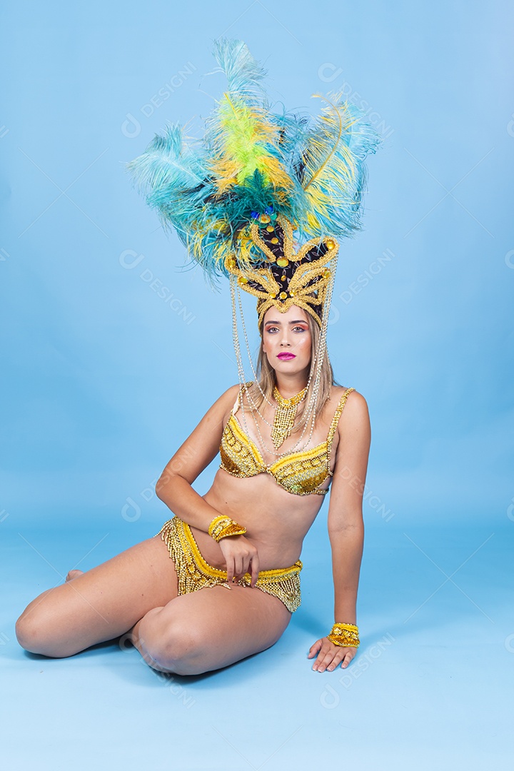 Linda passista loira fantasiada para o carnaval sentada no chão.