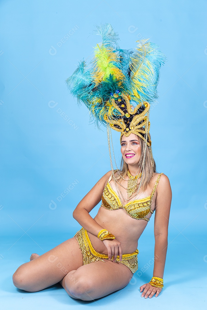 Linda passista loira fantasiada para o carnaval sentada no chão.