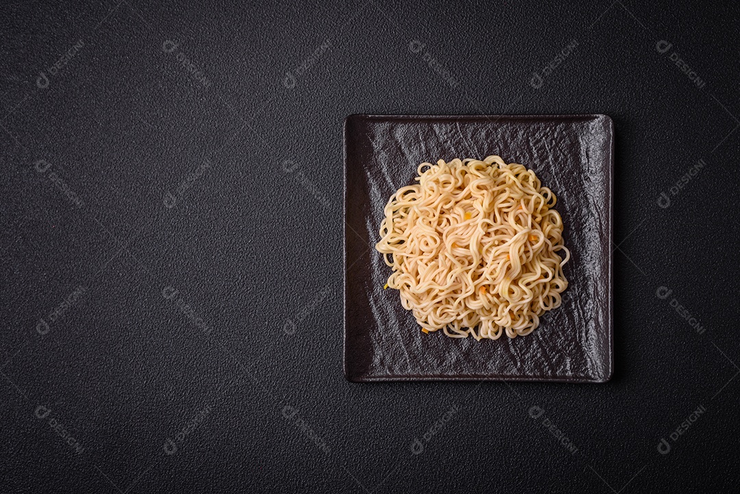 Delicioso prato de cozinha asiática com macarrão de arroz, pimentão, cogumelos e especiarias sobre fundo escuro de concreto
