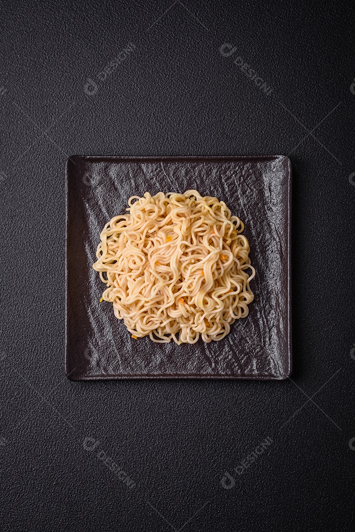 Delicioso prato de cozinha asiática com macarrão de arroz, pimentão, cogumelos e especiarias sobre fundo escuro de concreto
