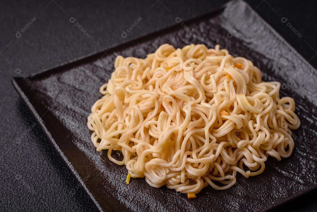 Delicioso prato de cozinha asiática com macarrão de arroz, pimentão, cogumelos e especiarias sobre fundo escuro de concreto