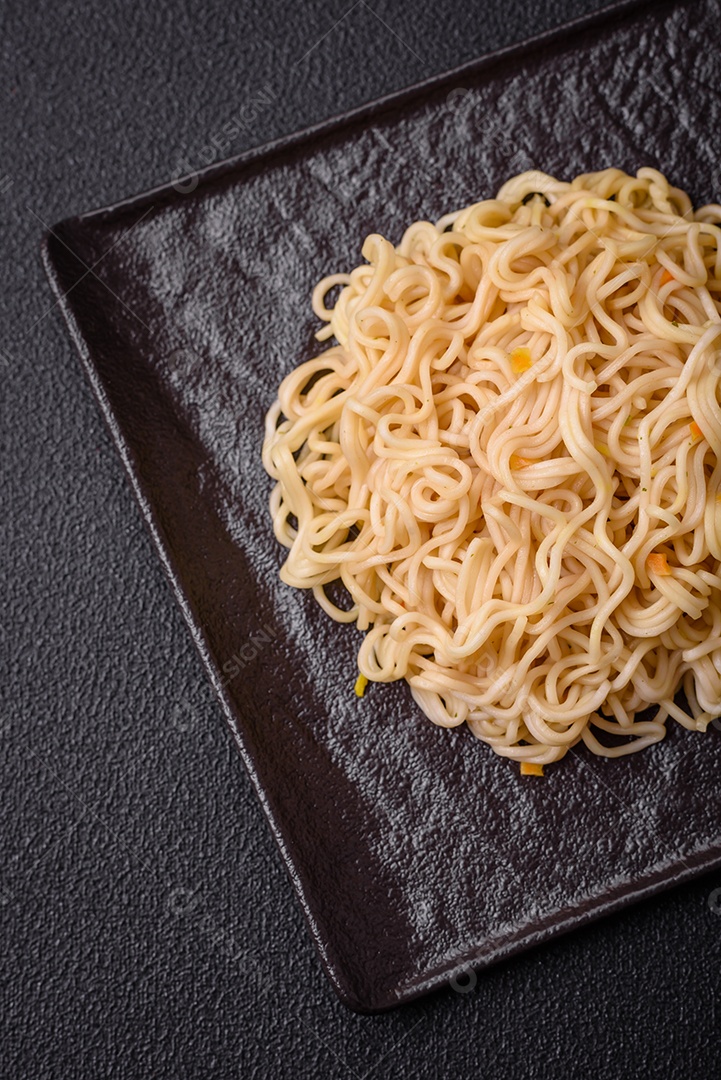 Delicioso prato de cozinha asiática com macarrão de arroz, pimentão, cogumelos e especiarias sobre fundo escuro de concreto
