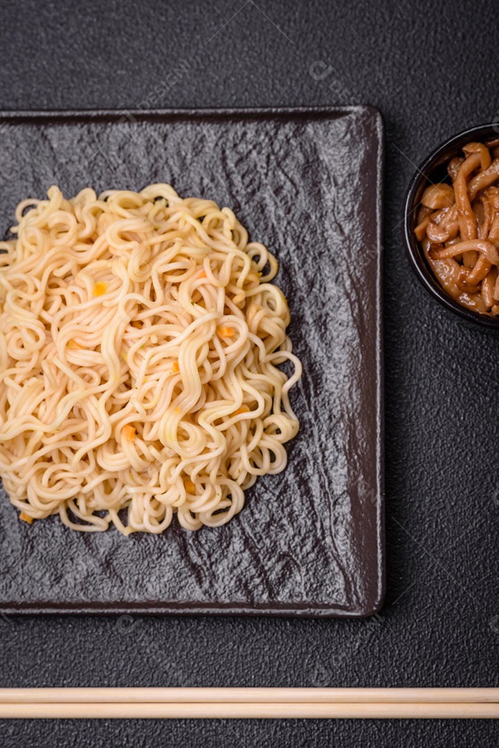 Delicioso prato de cozinha asiática com macarrão de arroz, pimentão, cogumelos e especiarias sobre fundo escuro de concreto