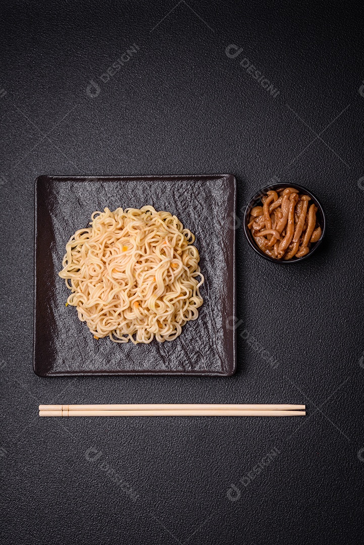 Delicioso prato de cozinha asiática com macarrão de arroz, pimentão, cogumelos e especiarias sobre fundo escuro de concreto