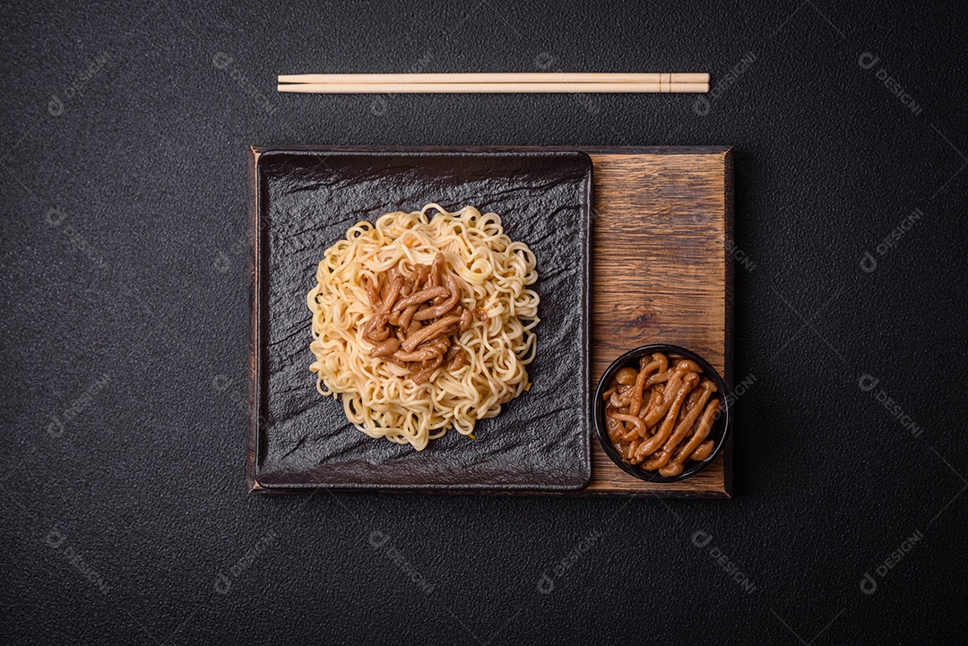 Delicioso prato de cozinha asiática com macarrão de arroz, pimentão, cogumelos e especiarias sobre fundo escuro de concreto