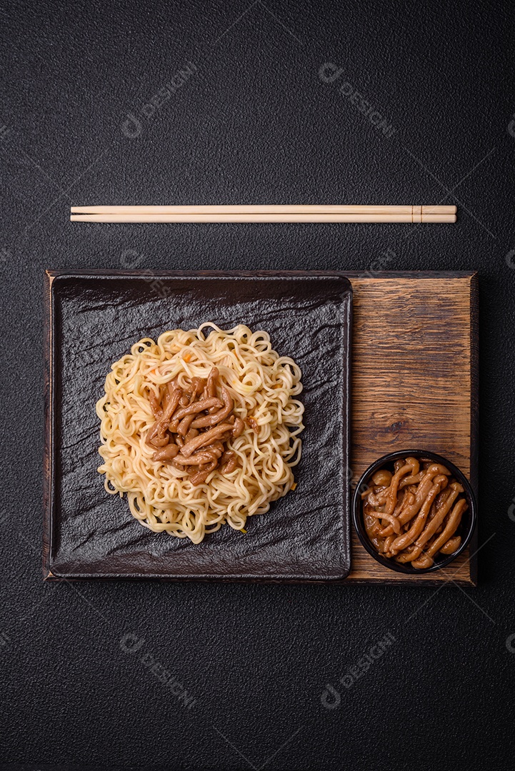Delicioso prato de cozinha asiática com macarrão de arroz, pimentão, cogumelos e especiarias sobre fundo escuro de concreto