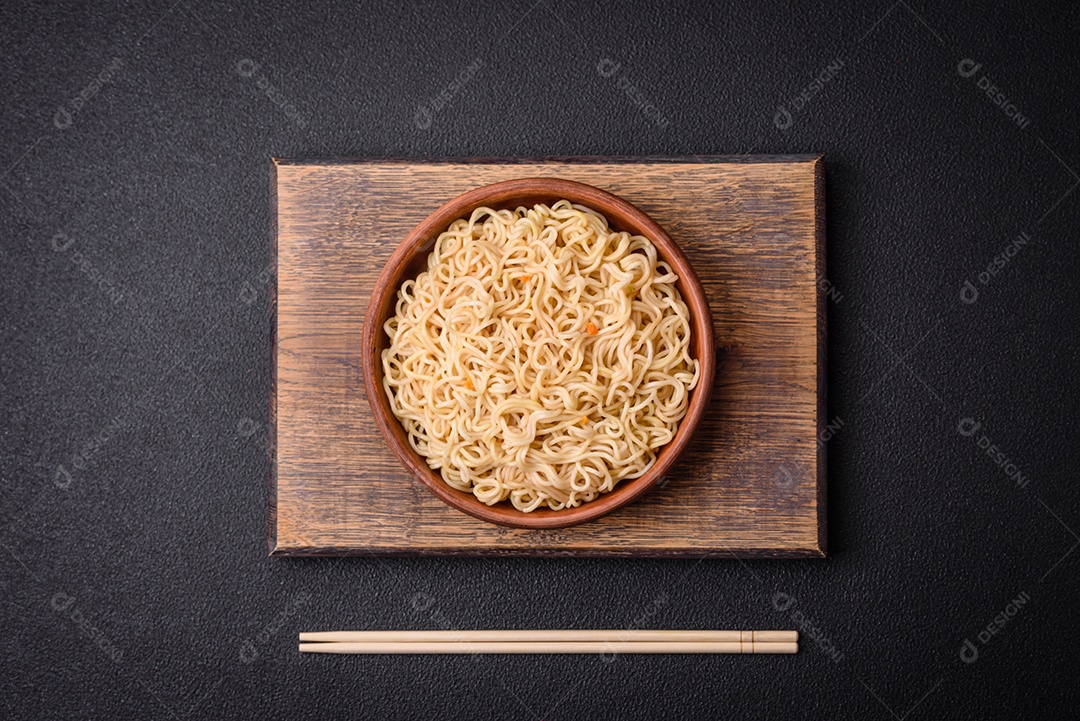 Delicioso prato de cozinha asiática com macarrão de arroz, pimentão, cogumelos e especiarias sobre fundo escuro de concreto