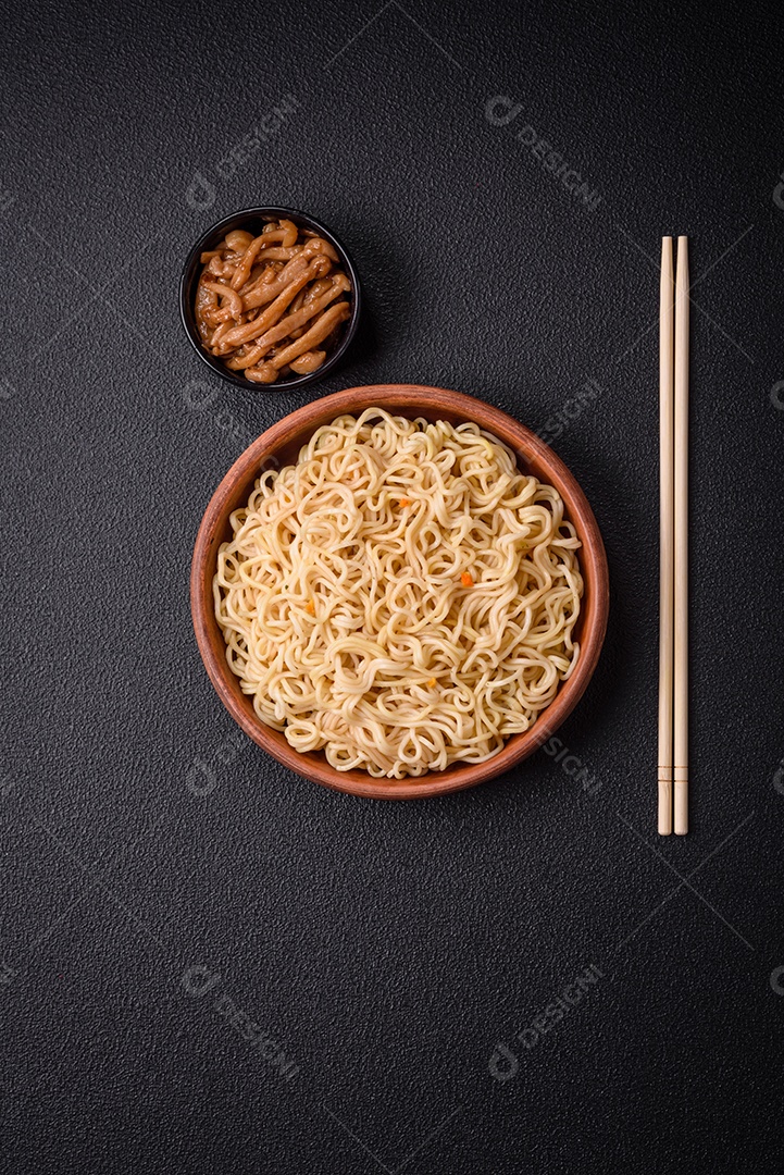 Delicioso prato de cozinha asiática com macarrão de arroz, pimentão, cogumelos e especiarias sobre fundo escuro de concreto