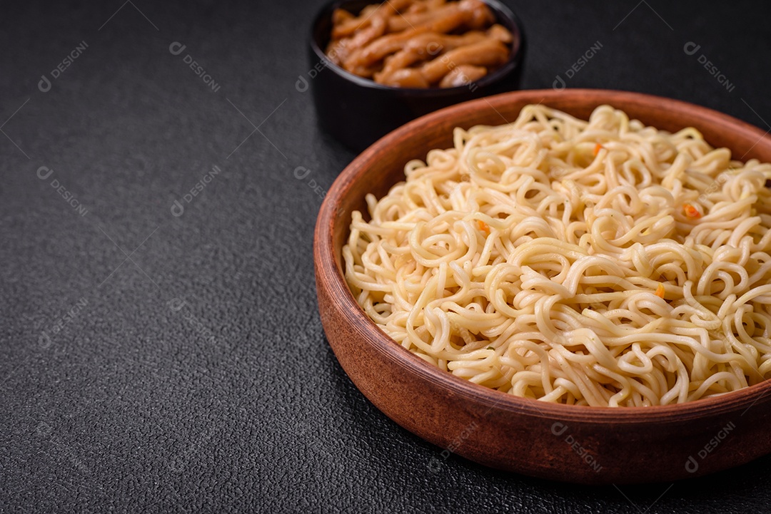 Delicioso prato de cozinha asiática com macarrão de arroz, pimentão, cogumelos e especiarias sobre fundo escuro de concreto
