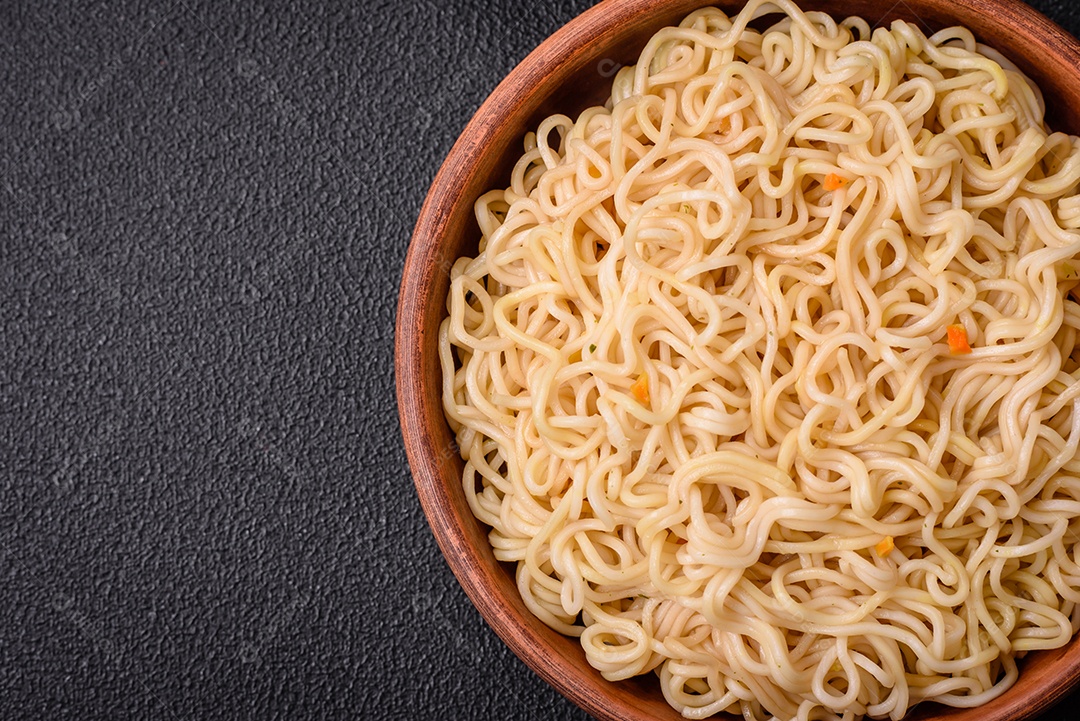 Delicioso prato de cozinha asiática com macarrão de arroz, pimentão, cogumelos e especiarias sobre fundo escuro de concreto