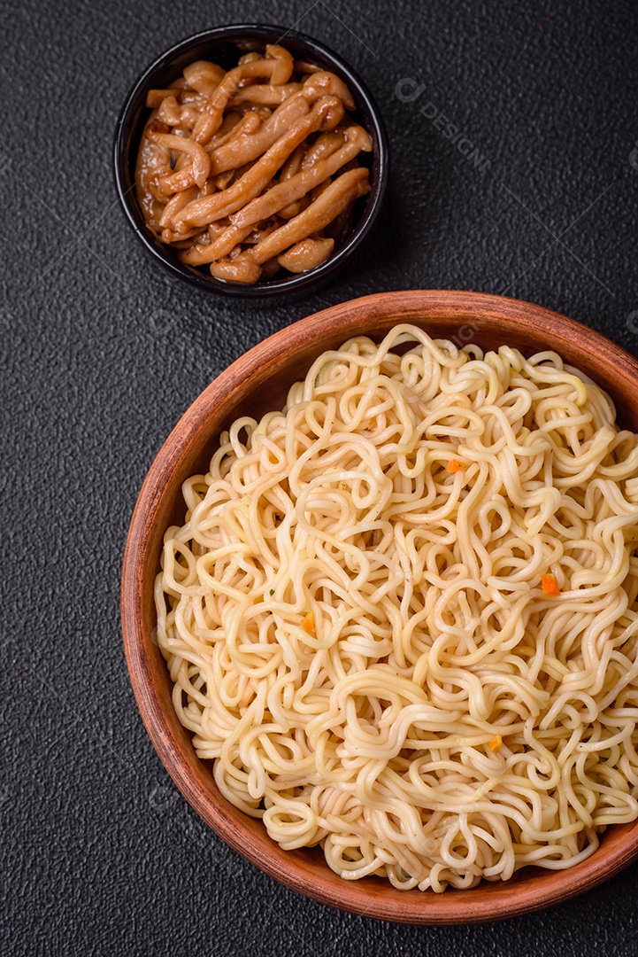 Delicioso prato de cozinha asiática com macarrão de arroz, pimentão, cogumelos e especiarias sobre fundo escuro de concreto