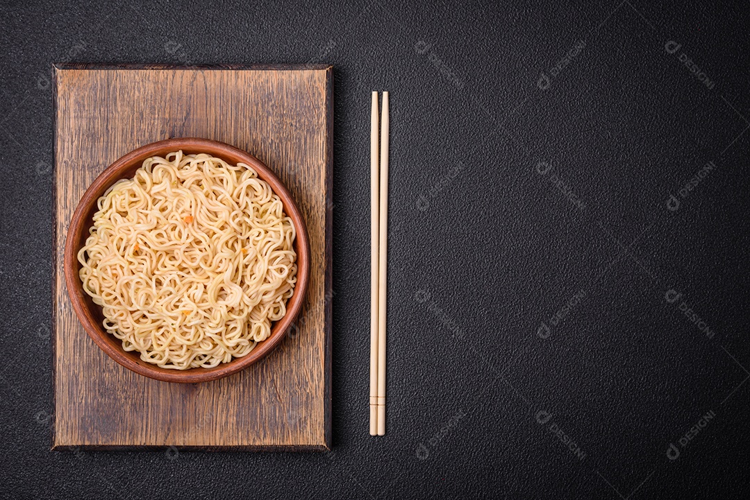 Delicioso prato de cozinha asiática com macarrão de arroz, pimentão, cogumelos e especiarias sobre fundo escuro de concreto