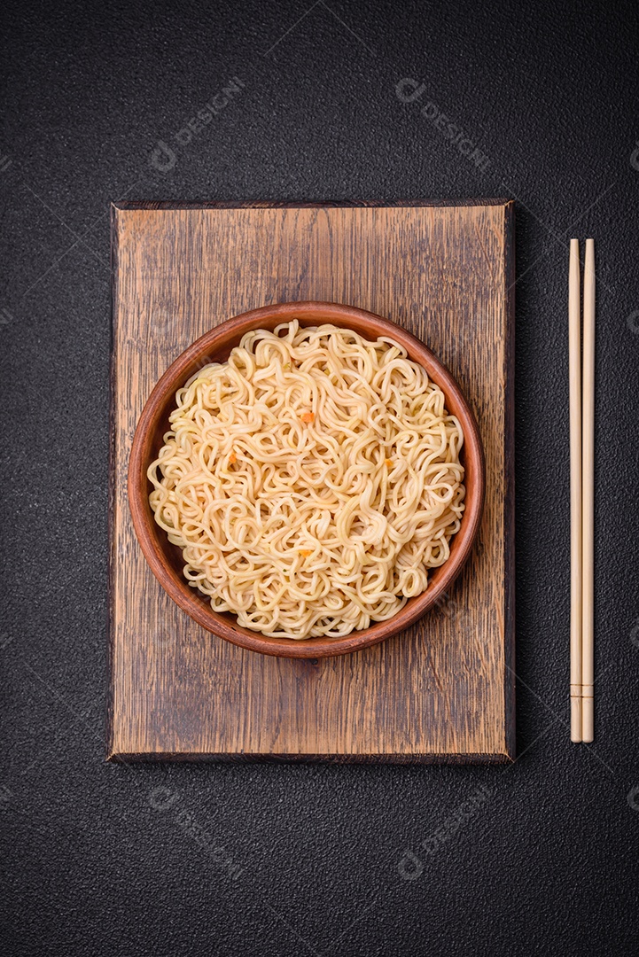 Delicioso prato de cozinha asiática com macarrão de arroz, pimentão, cogumelos e especiarias sobre fundo escuro de concreto