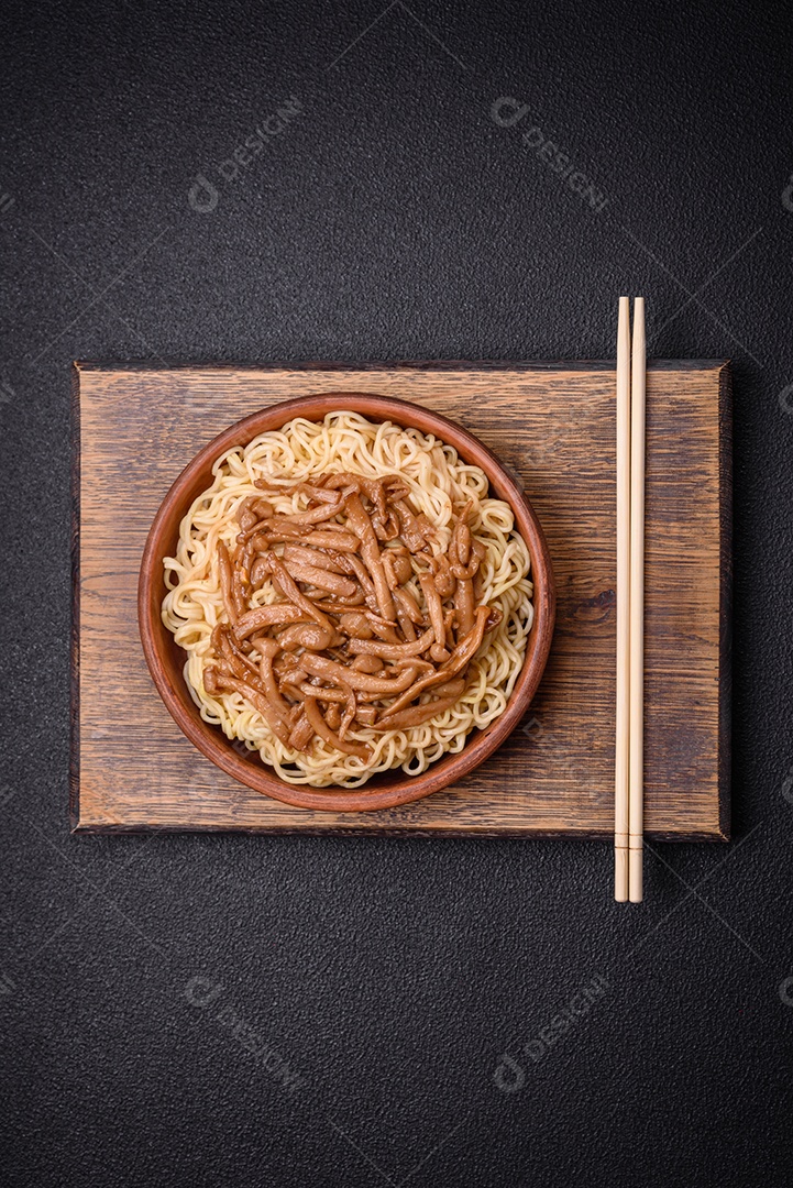 Delicioso prato de cozinha asiática com macarrão de arroz, pimentão, cogumelos e especiarias sobre fundo escuro de concreto