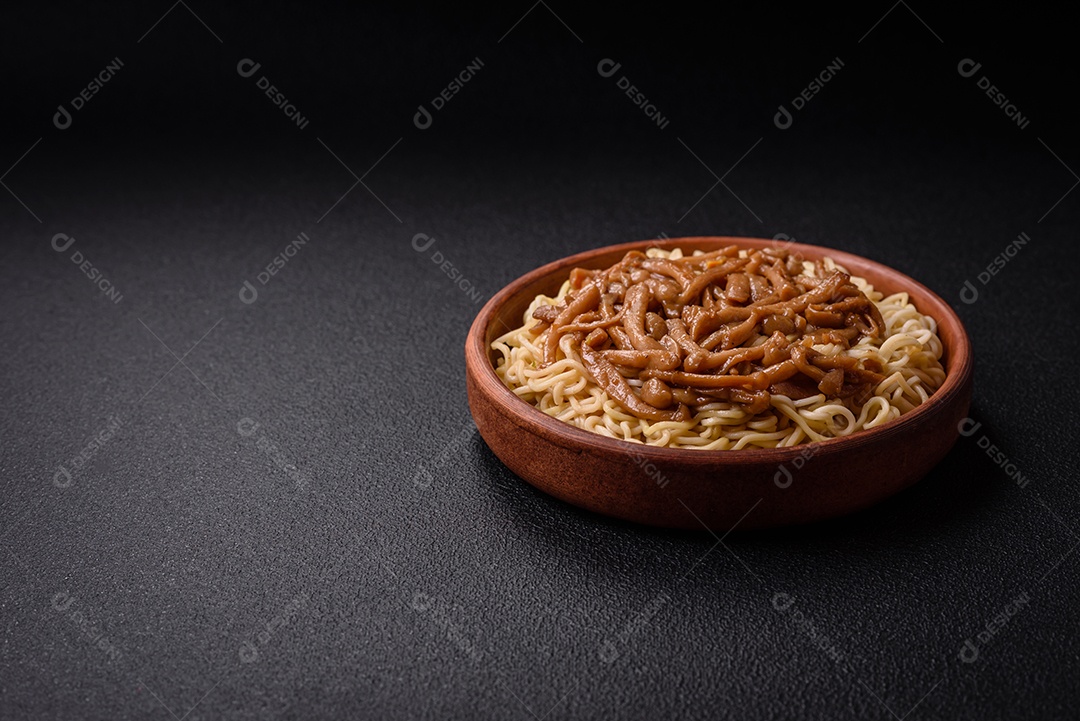 Delicioso prato de cozinha asiática com macarrão de arroz, pimentão, cogumelos e especiarias sobre fundo escuro de concreto