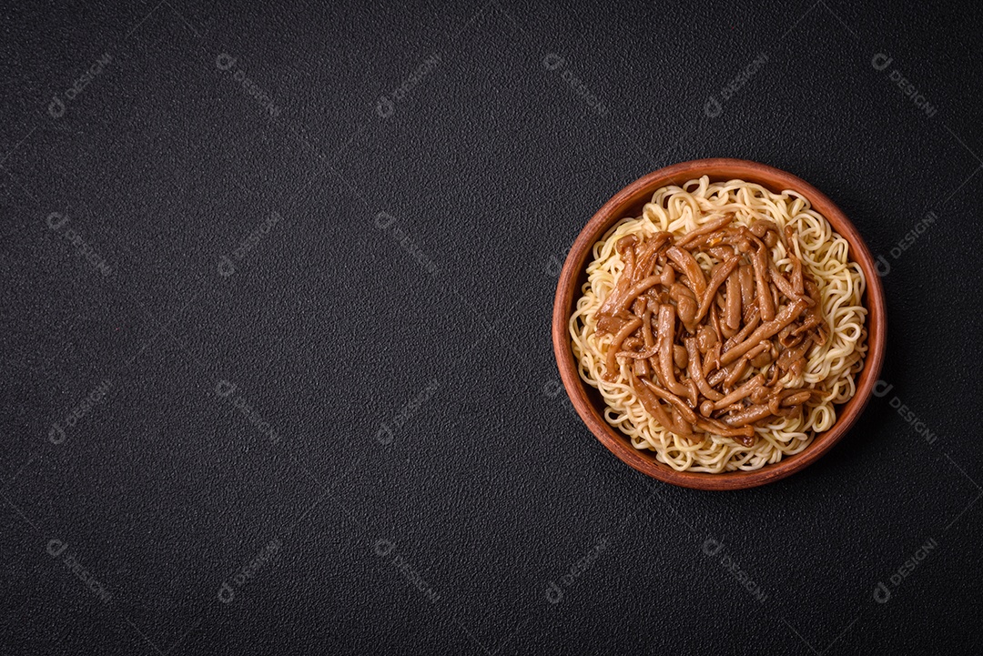 Delicioso prato de cozinha asiática com macarrão de arroz, pimentão, cogumelos e especiarias sobre fundo escuro de concreto