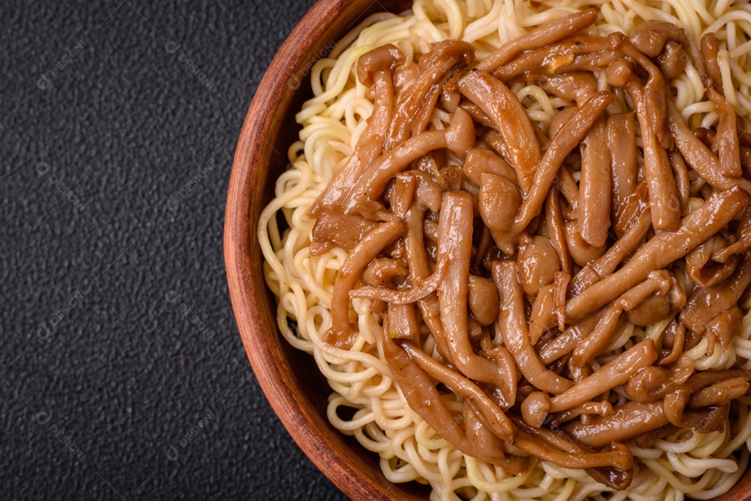 Delicioso prato de cozinha asiática com macarrão de arroz, pimentão, cogumelos e especiarias sobre fundo escuro de concreto