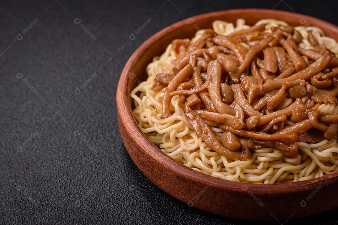Delicioso prato de cozinha asiática com macarrão de arroz, pimentão, cogumelos e especiarias sobre fundo escuro de concreto