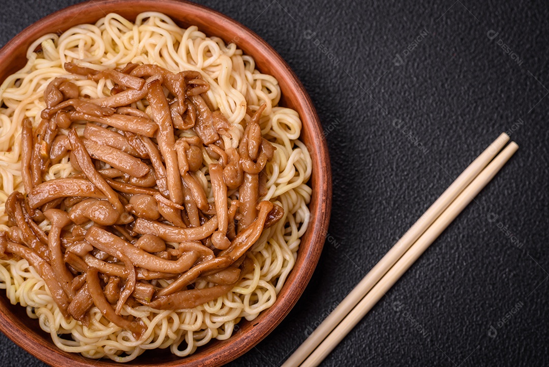 Delicioso prato de cozinha asiática com macarrão de arroz, pimentão, cogumelos e especiarias sobre fundo escuro de concreto