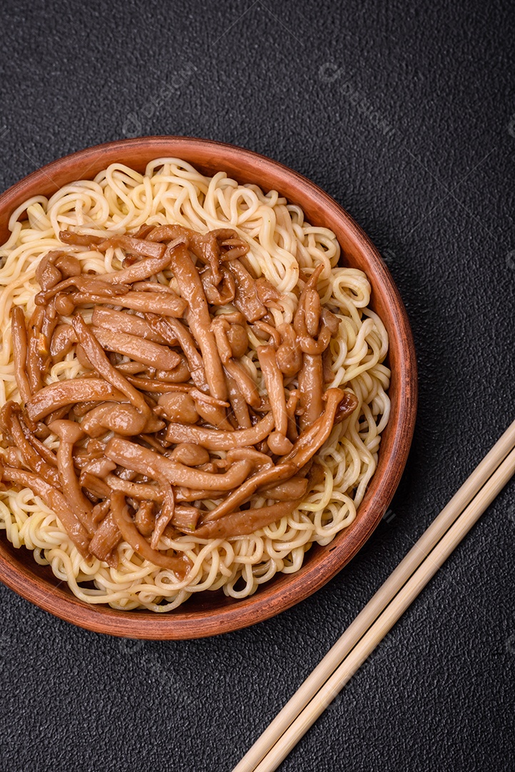 Delicioso prato de cozinha asiática com macarrão de arroz, pimentão, cogumelos e especiarias sobre fundo escuro de concreto