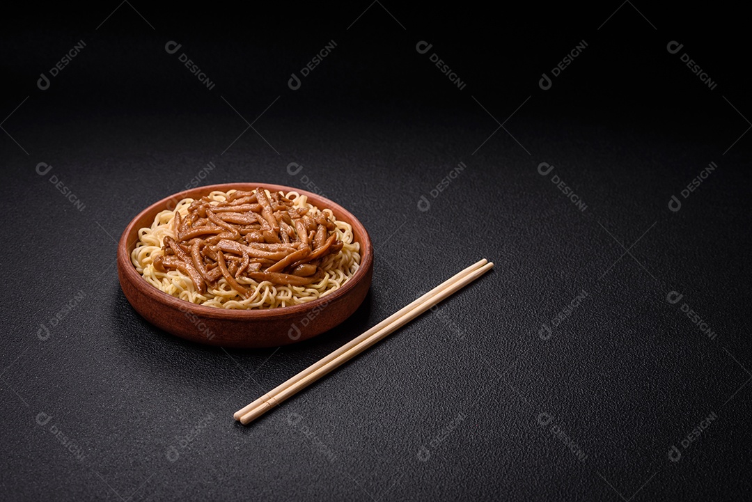 Delicioso prato de cozinha asiática com macarrão de arroz, pimentão, cogumelos e especiarias sobre fundo escuro de concreto