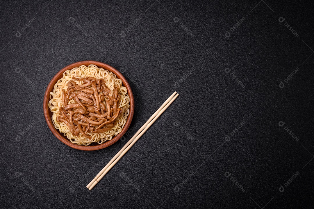 Delicioso prato de cozinha asiática com macarrão de arroz, pimentão, cogumelos e especiarias sobre fundo escuro de concreto
