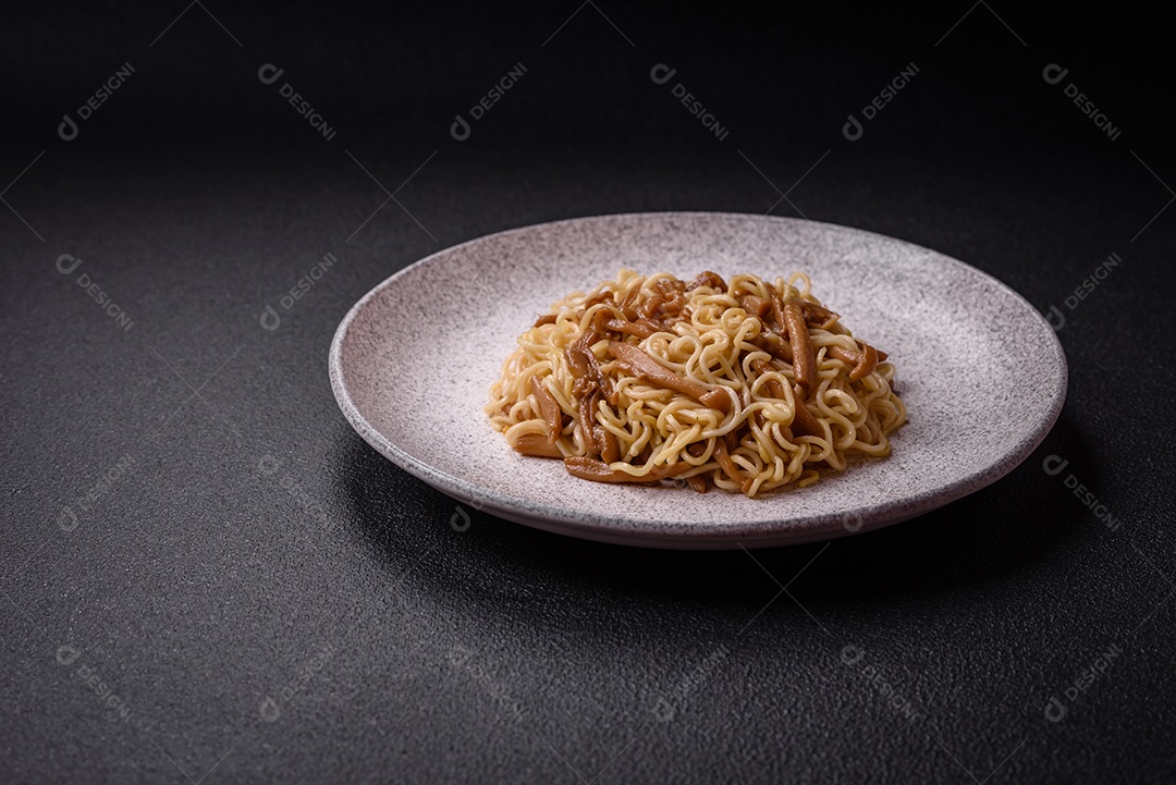 Delicioso prato de cozinha asiática com macarrão de arroz, pimentão, cogumelos e especiarias sobre fundo escuro de concreto