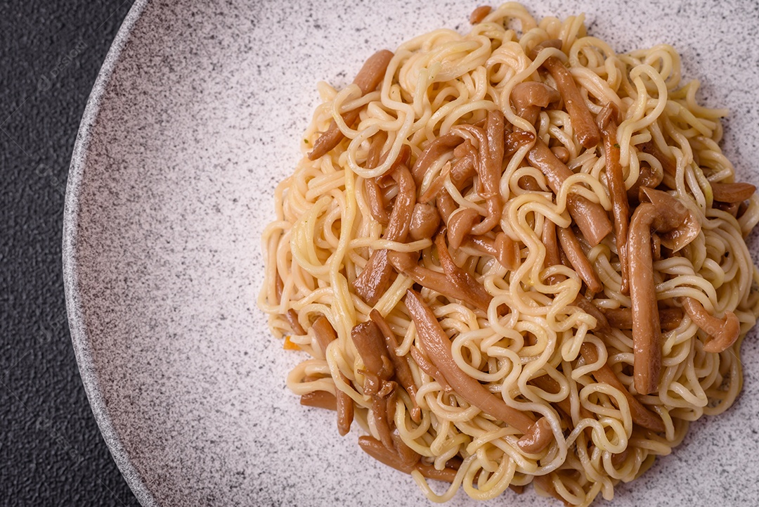 Delicioso prato de cozinha asiática com macarrão de arroz, pimentão, cogumelos e especiarias sobre fundo escuro de concreto