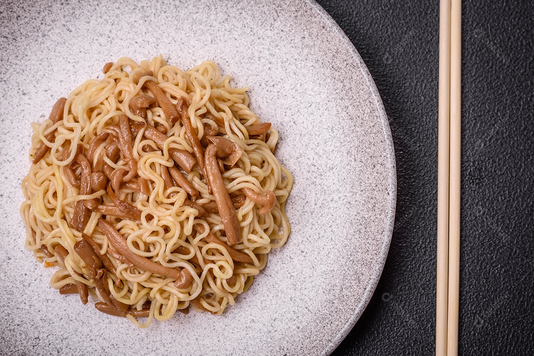Delicioso prato de cozinha asiática com macarrão de arroz, pimentão, cogumelos e especiarias sobre fundo escuro de concreto