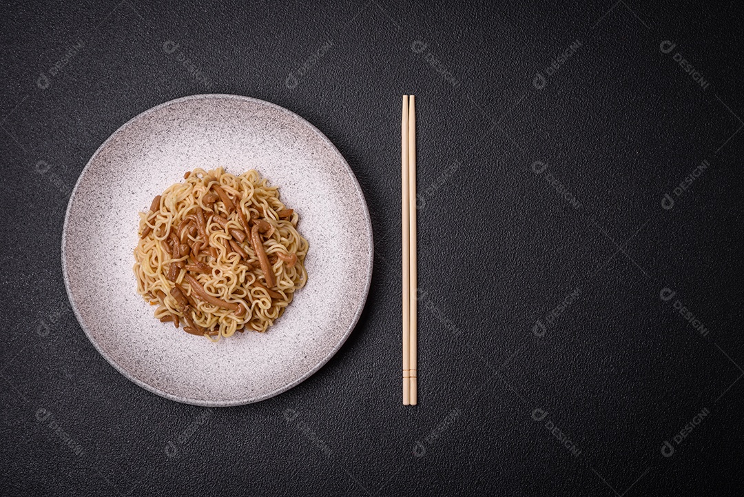 Delicioso prato de cozinha asiática com macarrão de arroz, pimentão, cogumelos e especiarias sobre fundo escuro de concreto