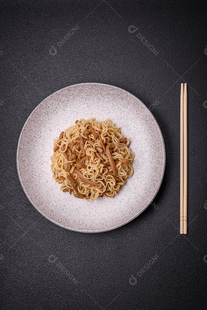 Delicioso prato de cozinha asiática com macarrão de arroz, pimentão, cogumelos e especiarias sobre fundo escuro de concreto
