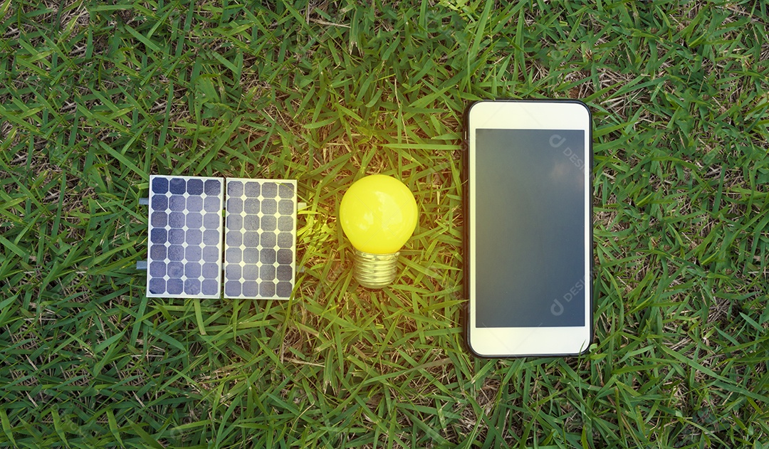 Segurando um fio de lâmpada e smartphone ao lado de um painel solar fotovoltaico em fundo de grama