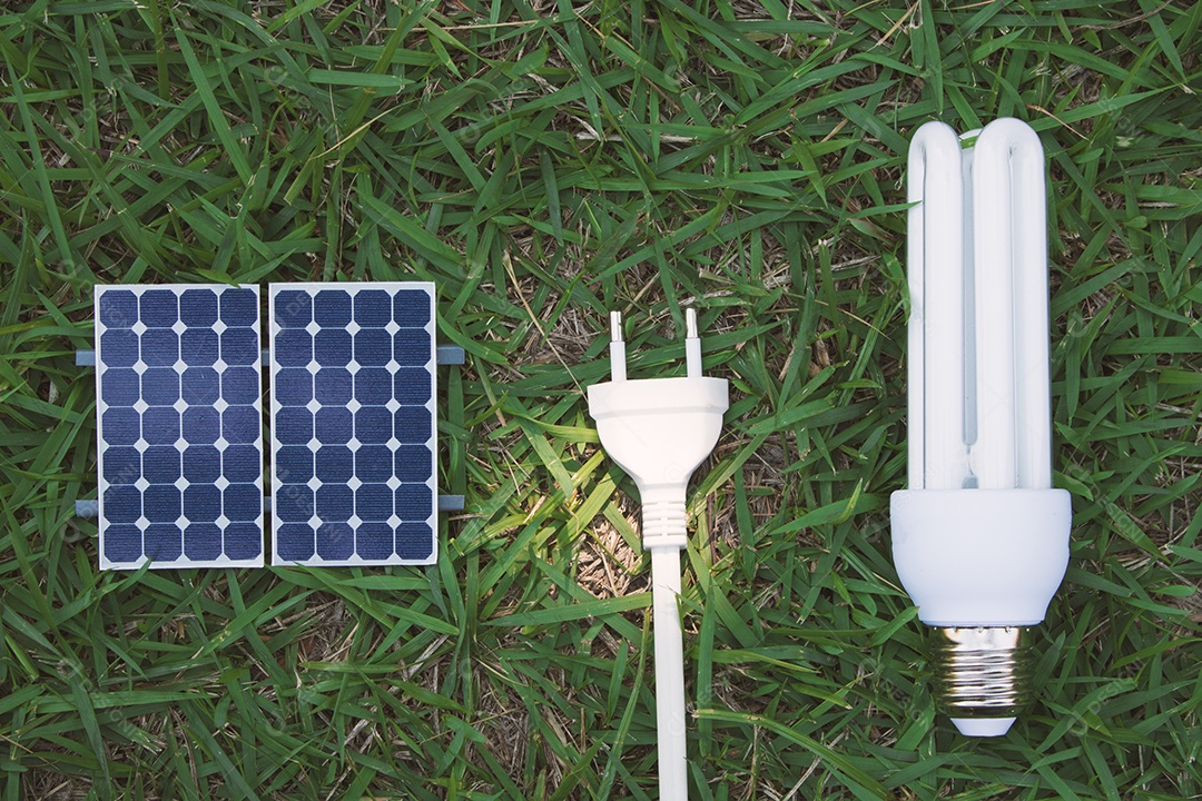 Segurando um fio de tomada e lâmpada ao lado de um painel solar fotovoltaico em fundo de grama