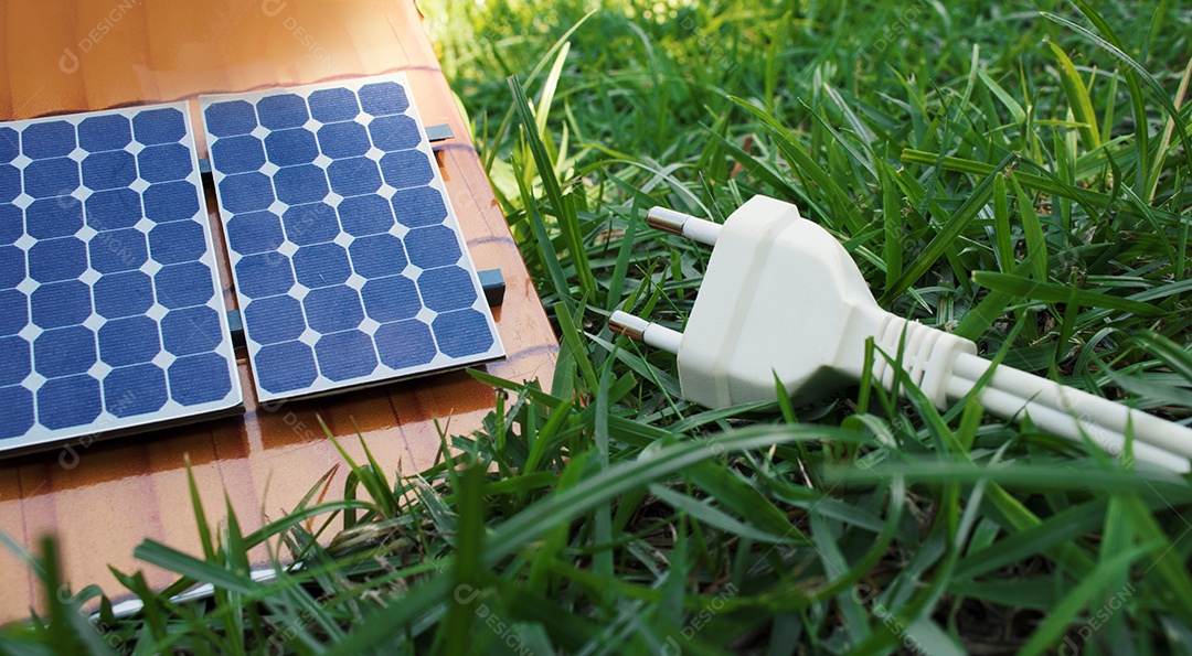 Segurando um fio de tomada ao lado de um painel solar fotovoltaico em fundo de grama