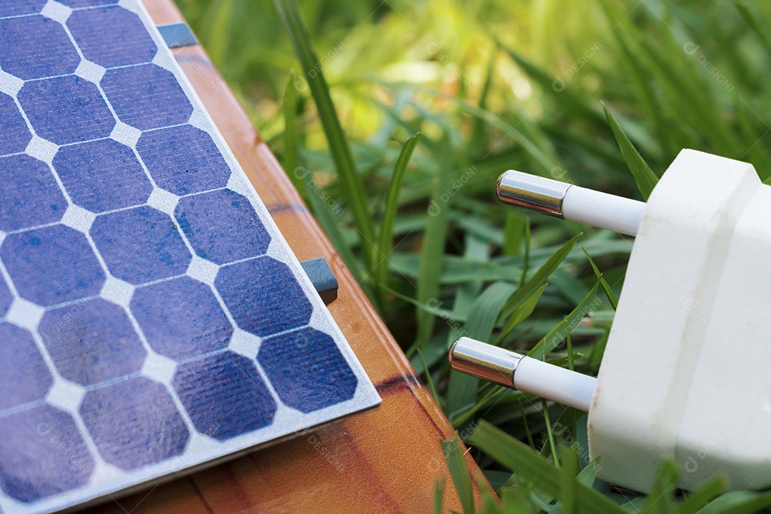 Segurando um fio de tomada ao lado de um painel solar fotovoltaico em fundo de grama