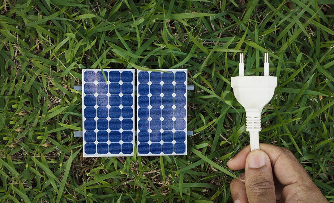 Segurando um fio de tomada ao lado de um painel solar fotovoltaico em fundo de grama