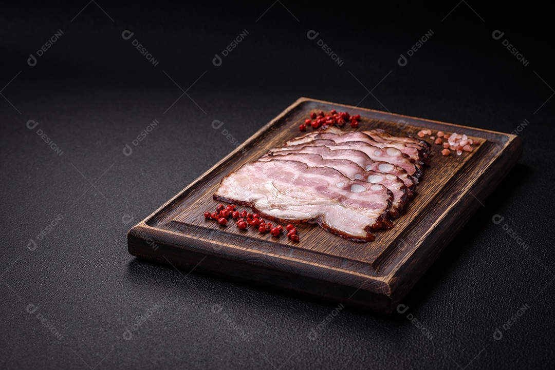 Deliciosa pancetta fresca ou bacon com sal e especiarias cortadas em fatias finas sobre um fundo escuro de concreto