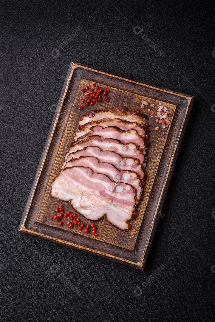 Deliciosa pancetta fresca ou bacon com sal e especiarias cortadas em fatias finas sobre um fundo escuro de concreto