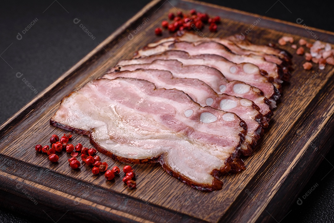 Deliciosa pancetta fresca ou bacon com sal e especiarias cortadas em fatias finas sobre um fundo escuro de concreto