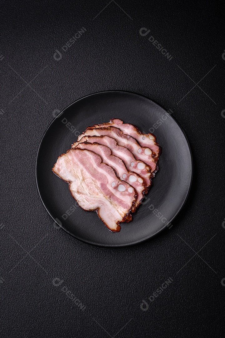 Deliciosa pancetta fresca ou bacon com sal e especiarias cortadas em fatias finas sobre um fundo escuro de concreto
