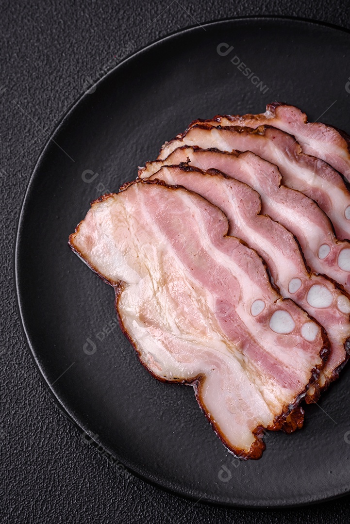 Deliciosa pancetta fresca ou bacon com sal e especiarias cortadas em fatias finas sobre um fundo escuro de concreto
