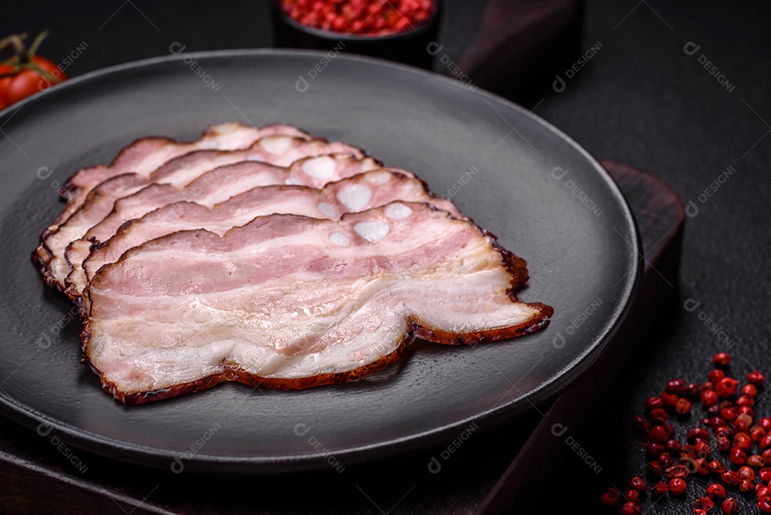 Deliciosa pancetta fresca ou bacon com sal e especiarias cortadas em fatias finas sobre um fundo escuro de concreto