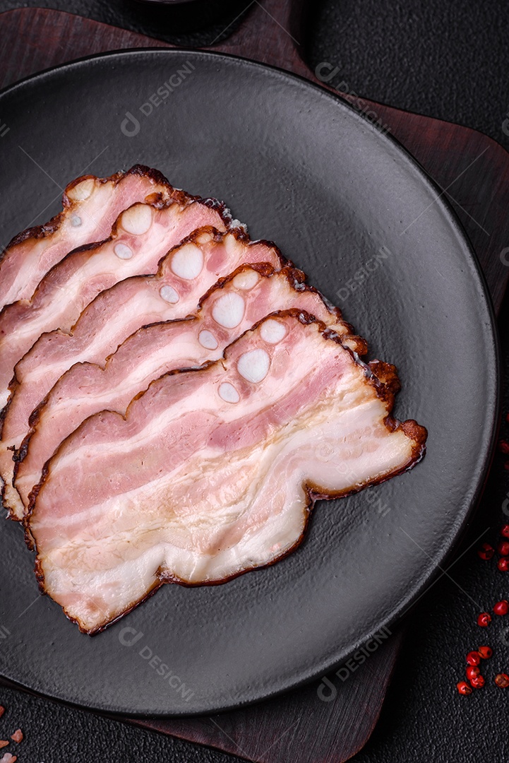 Deliciosa pancetta fresca ou bacon com sal e especiarias cortadas em fatias finas sobre um fundo escuro de concreto