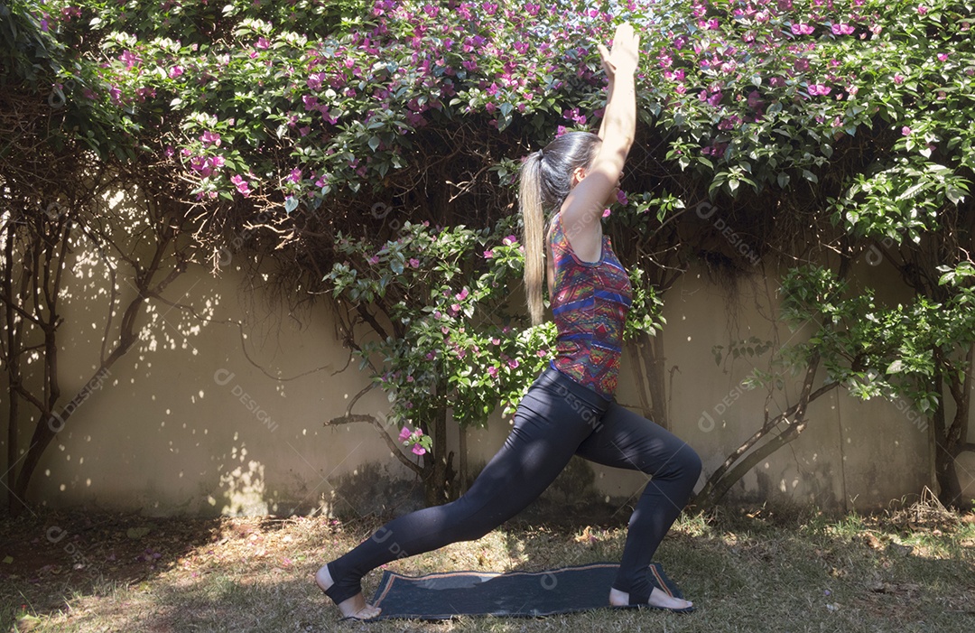Jovem brasileira praticando ioga no jardim da casa com sol e flores Imagem conceitual de ioga