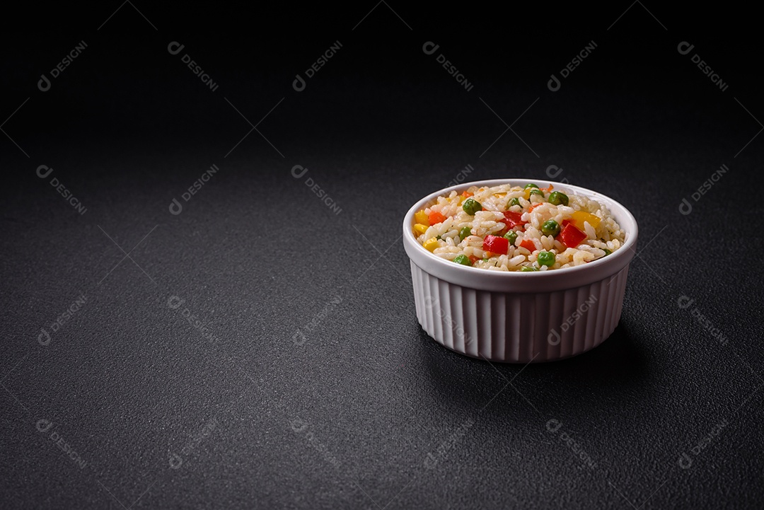 Delicioso arroz cozido branco com legumes, pimentões, cenouras, ervilhas, sal e especiarias sobre um fundo escuro de concreto