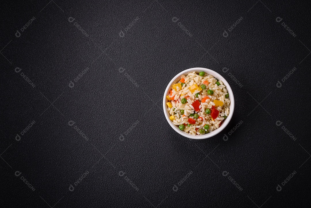 Delicioso arroz cozido branco com legumes, pimentões, cenouras, ervilhas, sal e especiarias sobre um fundo escuro de concreto