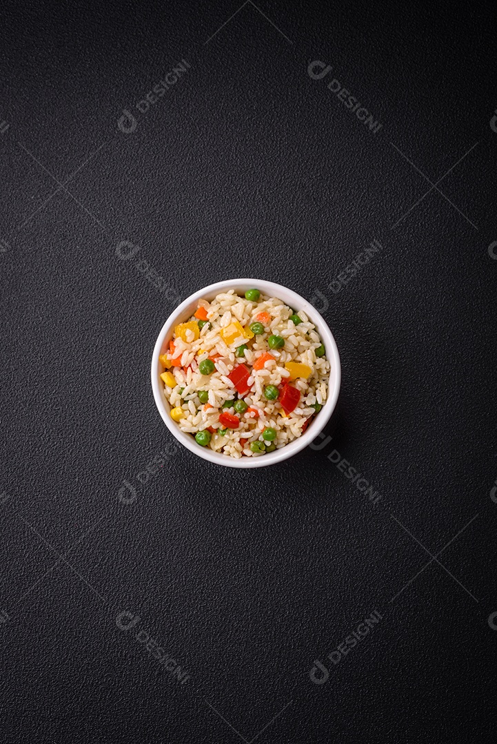 Delicioso arroz cozido branco com legumes, pimentões, cenouras, ervilhas, sal e especiarias sobre um fundo escuro de concreto