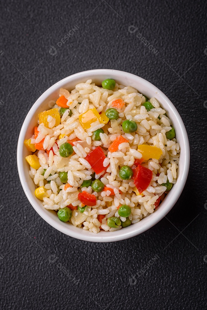 Delicioso arroz cozido branco com legumes, pimentões, cenouras, ervilhas, sal e especiarias sobre um fundo escuro de concreto