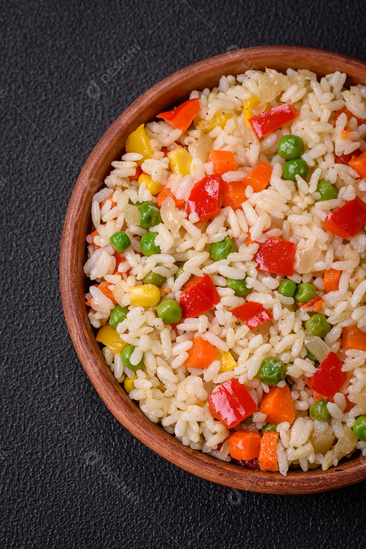 Delicioso arroz cozido branco com legumes, pimentões, cenouras, ervilhas, sal e especiarias sobre um fundo escuro de concreto