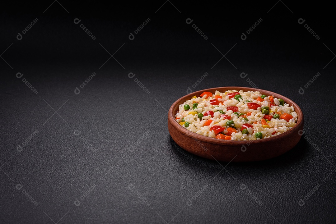 Delicioso arroz cozido branco com legumes, pimentões, cenouras, ervilhas, sal e especiarias sobre um fundo escuro de concreto